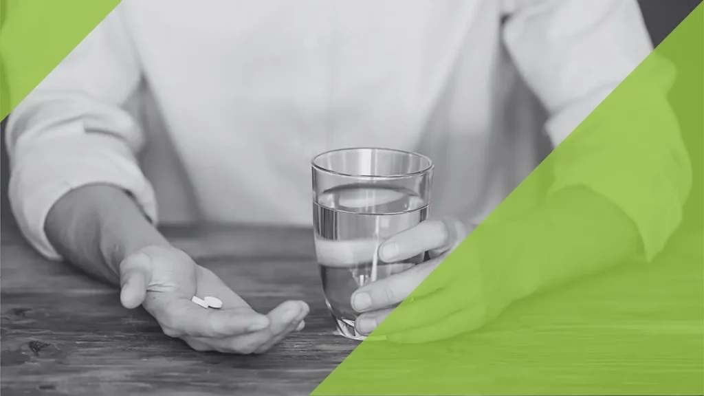 Twee handen, een tablet in de ene hand en een glas water in de andere hand