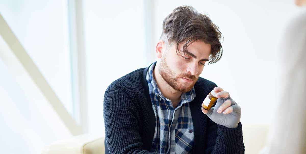 Afbeelding van een persoon in een peinzende houding die een pillendoosje vasthoudt om de keuze tussen medicatie en alternatieve behandelmethoden te illustreren.