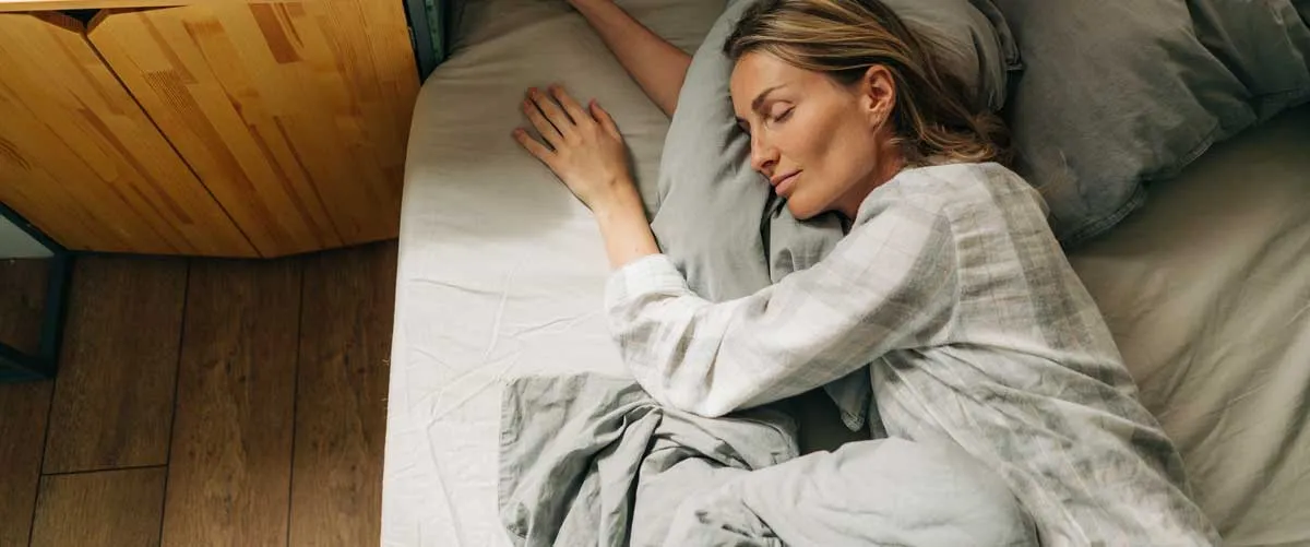 Beeld van een vredige slaapscène met een persoon die diep en rustig slaapt in een donkere, koele kamer. De afbeelding is bedoeld om het belang weer te geven van een rustige en ontspannen slaapomgeving voor het verbeteren van de slaapkwaliteit en het onder controle houden van de bloeddruk. Details zoals de afwezigheid van schermen en de nadruk op een donkere, rustige omgeving benadrukken de aanbevolen maatregelen voor een rustgevende slaap.