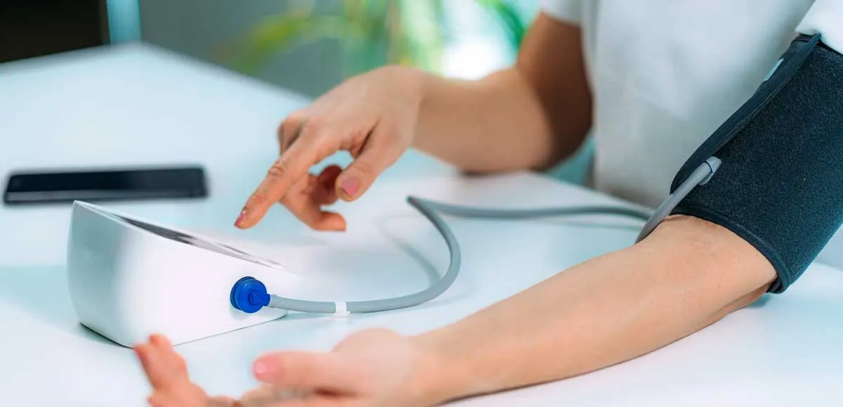 Een close-up van een persoon die een bloeddrukmeter om zijn arm draagt en wacht tot de meting is voltooid. Het apparaat staat in focus en benadrukt het belang van regelmatige bloeddrukcontrole.